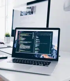 A MacBook with lines of code on its screen on a busy desk